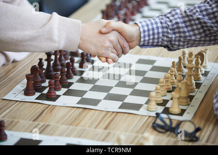 Two man shaking hands above table chess board and glasses before game at chess tournament Stock Photo