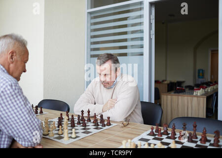 Two aged experienced grandmasters practicing chess skills by playing together at chess club Stock Photo