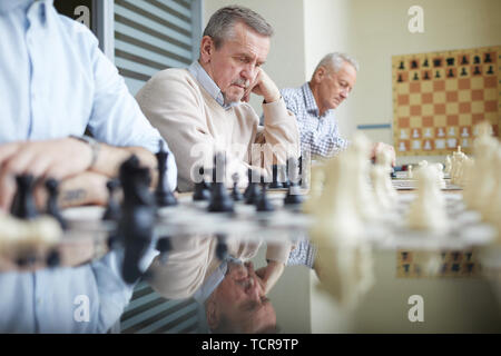 Long chess table in classroom at chess club with three chess players sitting in row next to different chess boards Stock Photo