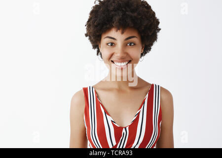 Waist-up shot of charming friendly-looking African American woman in striped blouse smiling joyfully and gazing at camera polite and carefree listenin Stock Photo