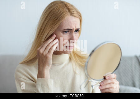 Mature Sad Woman Looking At Wrinkles In Mirror Stock Photo