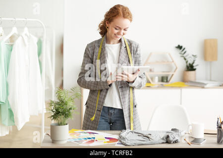 Smiling beautiful female fashion designer standing by dressmaker's model at  atelier stock photo