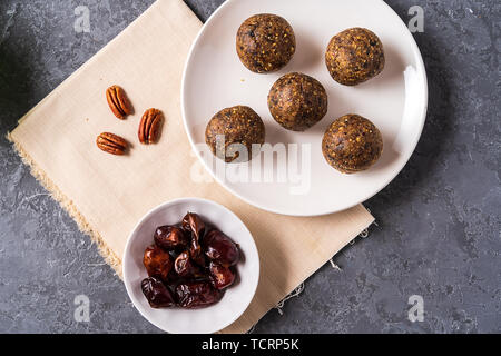 Healthy organic energy balls made with dates, oat flakes, dried cranberries, pecan nuts, in a plate on gray background, flat lay. Stock Photo