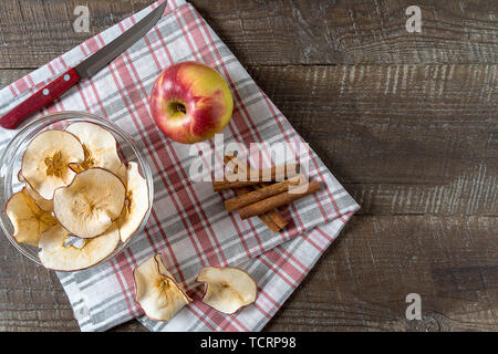Flat lay Dried apple chips , raw apple , cinnamon sticks on cooking board over wood background. Stock Photo