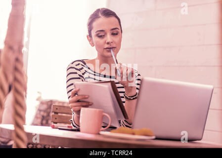 Woman wearing striped shirt feeling thoughtful holding pen and notebook Stock Photo