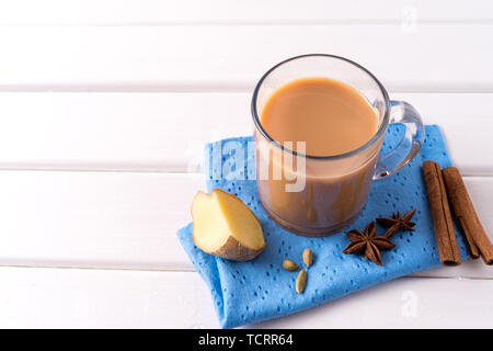 Indian traditional Masala chai tea in a glass and kitchen herbs, over white table background with copy space for text. Stock Photo