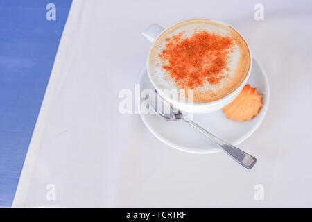 Brown colour of ground cinnamon on frosty whipping cream of Cappuccino cup in white ceramic mug on white blue table background.Cup Of Cappuccino With Stock Photo