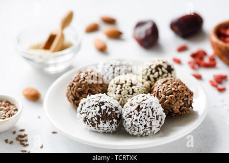 Tasty vegan protein truffles or candy or energy balls made with dates, nuts and seeds served on a white plate. Closeup view, selective focus