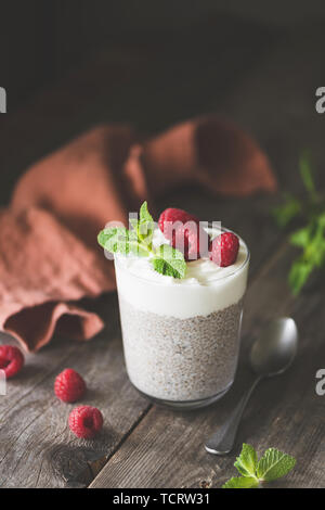 Chia pudding with raspberries in glass on wooden table. Toned image, vertical orientation Stock Photo