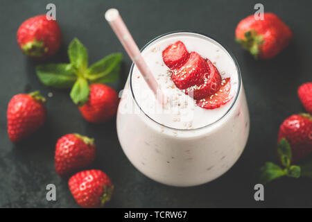 Strawberry milkshake or smoothie in glass with pink drinking straw on black background. Toned image Stock Photo