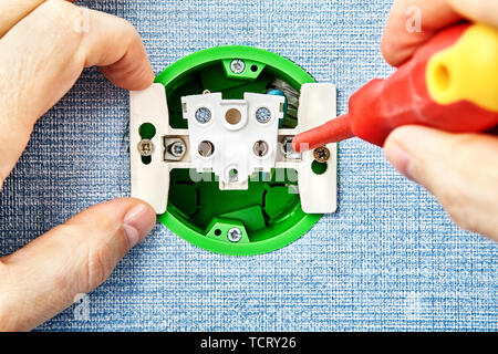 Electrical power point installation, electric socket  inside, electrician is fixing outlet module with screwdriver. Stock Photo