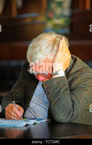 Senior man with head in hand concentrating on the puzzle pages of a daily newspaper Stock Photo