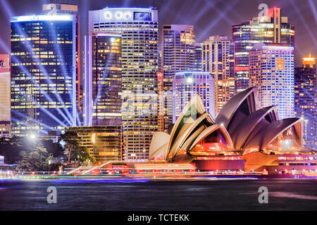 Facades of High-rise office towers of Sydney city CBD on waterfront of Sydney harbour illuminated by blue laser beams of Vivid Sydney light show. Stock Photo