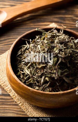 Heap of dried, raw white tea leaves in wooden bowl on bamboo mat background Stock Photo