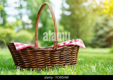 Empty picnic basket with red checkered napkin on the grass. Warm natural sunlight. Space for text. Stock Photo