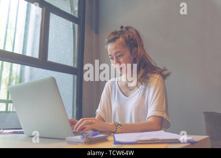 Young happy lady in white t-shirt using laptop while working  Stock Photo
