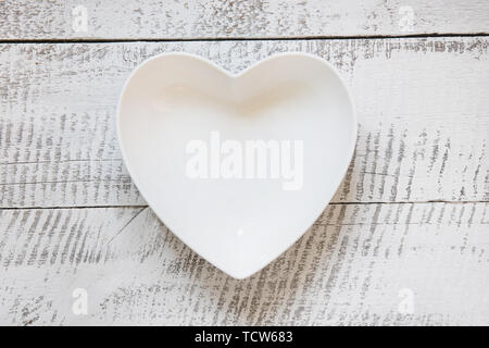 White plate in shape of heart on wooden vintage table. Top view. Space for text. View vrom above. Horizontal orientation. Stock Photo