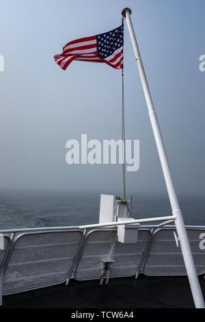 The stars and stripes fluttering at the top of a flag pole in the wind on the back of a ferry crossing to Canada, nobody in the image Stock Photo