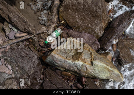 A single plastic bottle is washed up between rocks on the coastline of Ireland, nobody in the image Stock Photo