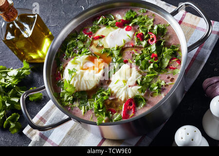 Fresh Homemade red kidney Bean Soup with poached eggs and cilantro in a metal pan on a concrete table with a wooden spoon and ingredients, view from a Stock Photo