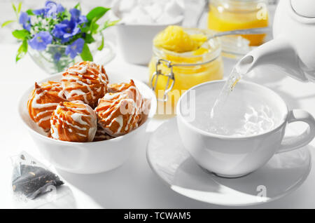 Cup of hot tea with cookies and honey on a white background. The process of pouring boiling water, tea bags. Flowers in the background, selective focu Stock Photo