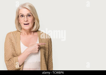 Amazed senior woman looking at camera pointing finger at copyspace Stock Photo
