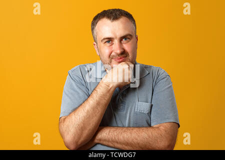 Pensive man holding hand on chin and looking at camera. Yellow background. Closeup portrait. Stock Photo