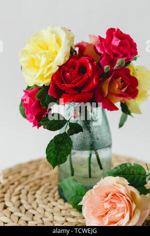 Coloful roses in vase on a nature wicker napkin on white background Stock Photo