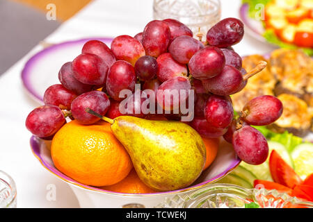 Fruit in a plate on the table. Bunch of grapes, pear and orange on the plate Stock Photo