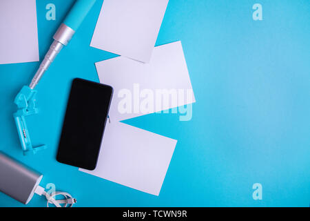 Smartphone with blank screen and flyers and photos on a blue background. Mock up, flat lay. Summer vacation concept. Stock Photo