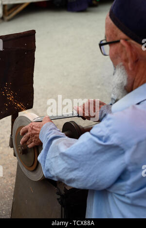 The man is sharpening traditional Uzbek knives on the street, Kokand bazaar. Stock Photo