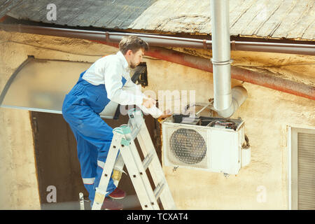 HVAC technician working on a capacitor part for condensing unit. Male worker or repairman in uniform repairing and adjusting conditioning system, diagnosting and looking for technical issues. Stock Photo