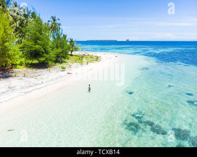 Aerial: Woman getting out of caribbean sea turquoise water tropical coral reef walking on white sand beach. Banyak Islands Sumatra Indonesia scenic tr Stock Photo