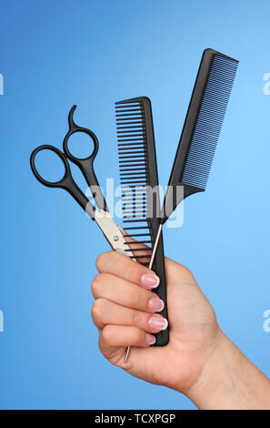 Color combs and scissors in female hand on color background Stock Photo