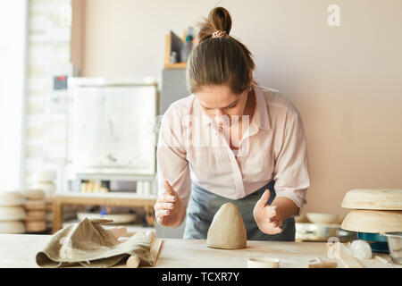 Waist up portrait of female potter shaping clay while working in studio, copy space Stock Photo