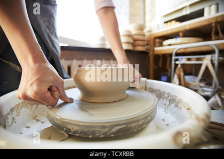 Closeup of female artisan cutting clay pot off potters wheel using string, copy space Stock Photo