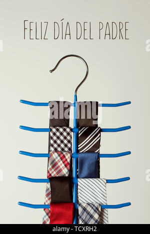 the text feliz dia del padre, happy fathers day written in spanish, and a necktie hanger with some neckties of different colors and patterns, on an of Stock Photo