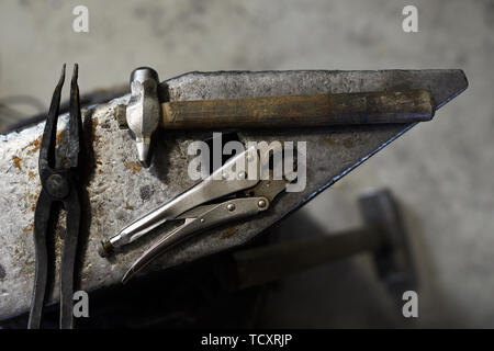 Above view of blacksmiths tools such as hammer, tongs and pliers on steel anvil in workshop Stock Photo
