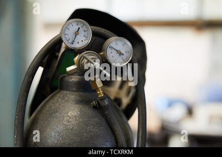 Close-up of air tank cylinder with tubes and pressure gauges, welding helmet hanging on gas cylinder Stock Photo