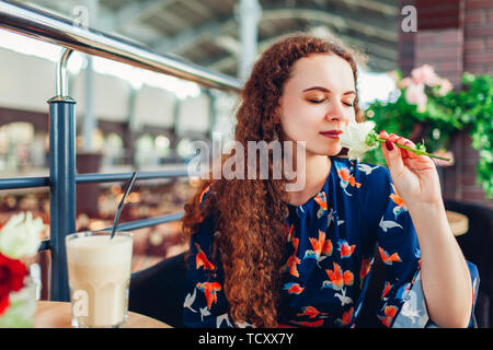 Young woman smelling rose in shopping center cafe while drinking coffee. Relaxing and enjoying life Stock Photo