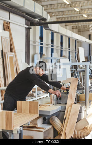 Carpenter working on an electric buzz saw cutting some boards, he is wearing black uniform and a cap. Vertical shot Stock Photo