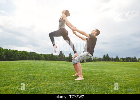 Strong and healthy. Young and beautiful couple practicing acro yoga on a grass in open field. Yoga in pair. Sunny morning. Partner yoga concept Stock Photo