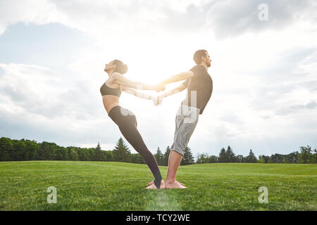 Yoga in pair. Beautiful young couple practicing acro yoga together and stretching in nature on a sunny morning. Healthy lifestyle. Partner yoga concep Stock Photo