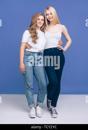 Portrait of lovable girls Full height image Two young friends in jeans, white t-shirts, and sneakers are standing hugging Stock Photo