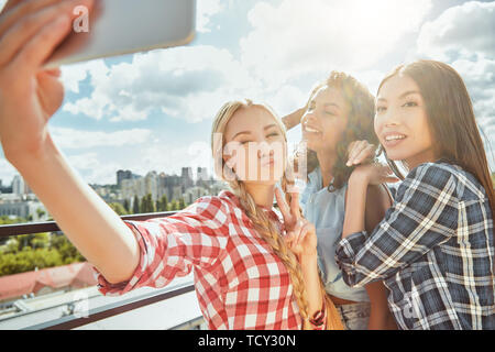 Funny selfie with friends! Group of cheerful and young women are making selfie and smiling at camera while having barbecue on the roof. Summer concept Stock Photo