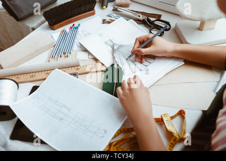 Making sketches at not pad. Close-up of young woman tailor with not pad is modeling new clothes in design studio Stock Photo