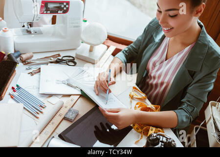 Making sketches at not pad. Close-up of young woman tailor with not pad is modeling new clothes in design studio Stock Photo