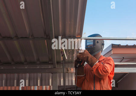 Worker welding in orange work clothes welding For roof truss Stock Photo