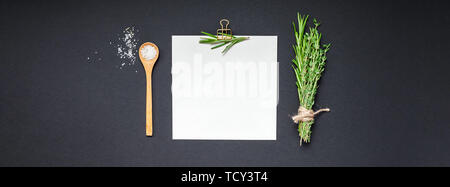 Flat lay overhead view blank recipe paper page with clip mockup text space invitation card on black background with greens herbs and spices. Menu reci Stock Photo