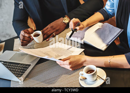 Close up of co-workers' table. They are having lunch at restaurant, discussing project. Man drinks his coffee, while woman presenting documents to him Stock Photo